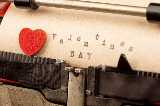 Happy Valentine`s day - phrase on typewriter. Valentines Day greetings concept. Little red wooden heart close up. Valentines greeting card.