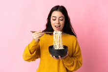 Young Caucasian Woman Isolated On Pink Background Holding A Bowl Of Noodles With Chopsticks