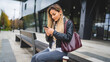 © Miljan Živković - one young caucasian woman female student sitting in front of the university in autumn day waiting while holding mobile phone reading messages or browsing internet real people copy space