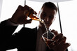 © Andriy Medvediuk - smiling male businessman in suit pours a glass of alcohol, cognac or whiskey, from a mini bottle in the hotel