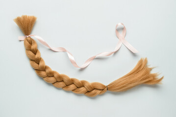 Braided red hair for donation with pink ribbon on light background