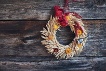 Wreath Of Golden Ears Of Wheat, Dried Flowers And Herbs Tied With Red Ribbon Hung On Wooden Wall