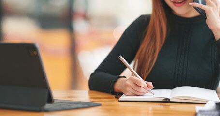 Wall Mural - young woman in black sweater writing business papers and using mobile phone at desk in modern coworking office. copy space