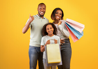 Wall Mural - Black friday concept. Happy black parents and cute daughter holding shopper bags, man showing thumb up