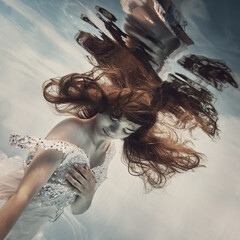 Wall Mural - A girl in a white dress with dark hair swims underwater as if flying