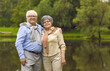 © Studio Romantic - Portrait of smiling elderly pensioners standing in the park by the lake in summer. Senior man and woman are resting outdoors in the park. Happy joyful penionaries having a rest in the park.