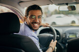 Fototapeta  - Cheerful middle-eastern taxi driver looking at back seat and smiling