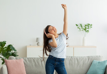 Wall Mural - Cheerful Indian teen girl with wireless headphones dancing to lovely music at home