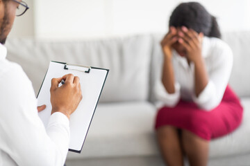 Wall Mural - Unhappy young black lady crying on consultation with psychotherapist at clinic