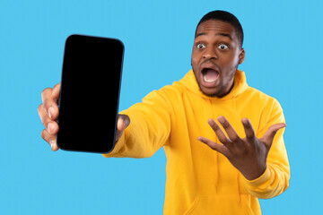 Emotional Black Guy Showing Smartphone With Empty Screen, Blue Background