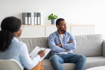 Wall Mural - Young psychologist working with emotionally detached black male patient at clinic, trying to help him with depression