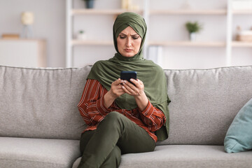 Wall Mural - Serious Muslim Woman Using Smartphone Frowning Reading News At Home