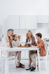 happy grandparents playing chess with kids in kitchen.