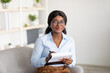 Friendly black female psychologist writing in clipboard, having session with client, sitting on couch at modern office
