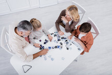 Overhead View Of Children With Grandparents Playing Jigsaw Puzzle Game On Kitchen Table.