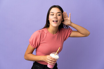 Wall Mural - Teenager girl holding a strawberry milkshake listening to something by putting hand on the ear