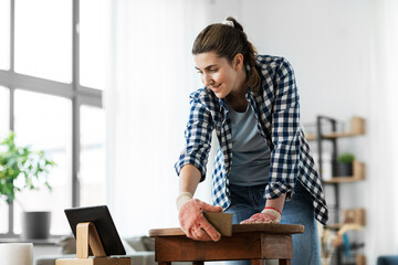 Wall Mural - furniture renovation, diy and home improvement concept - happy woman sanding old wooden table and looking at tablet pc computer with sponge