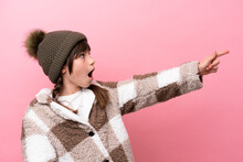 Little Caucasian Girl With Winter Jacket Isolated On Pink Background Pointing Away