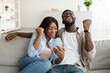 African american couple using smartphone, celebrating win