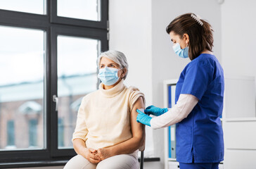 Sticker - medicine, health and vaccination concept - doctor or nurse applying medical patch to vaccinated senior woman in mask at hospital