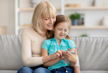 Wall Mural - Happy mature woman and granddaughter using cellphone