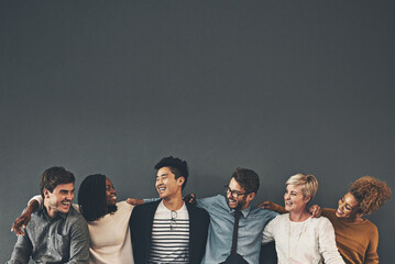 we make a great team. studio shot of a diverse group of creative employees embracing each other agai
