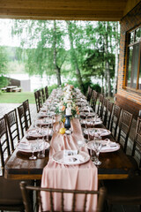 Wall Mural - A beautiful outdoor wedding setting in pink flowers. plates and cutlery on a wooden table against a backdrop of greenery. On a Summer day 
a wooden reception table in the backyard, decorated with rose