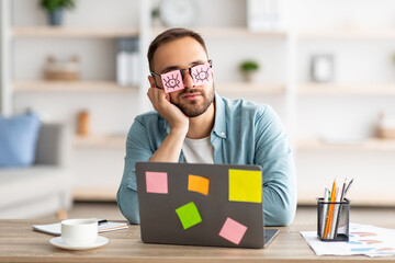 Poster - Tired young man having stickers with open eyes drawing on glasses, sleeping near laptop, pretending to work at office