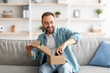 © Prostock-studio - Happy Caucasian man receiving package, unboxing parcel, taking out gaming joystick, sitting on sofa in living room