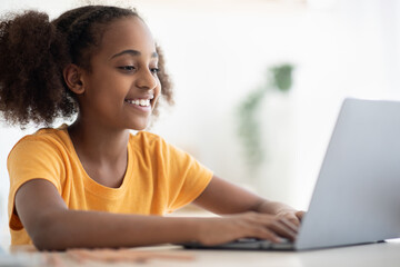 Joyful black girl studying online, using laptop, typing on keyboard