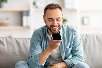 Poster - Cheerful millennial guy sitting on couch with cellphone at home, mockup for mobile app or website on screen