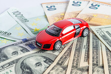 A Model Of A Beautiful Sports Car Stands On Dollar And Euro Bills Of Various Denominations.