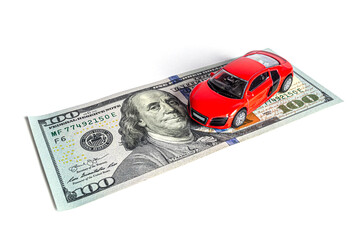 A close-up model of a beautiful sports car stands on a 100 American dollar bill isolated on a white background.