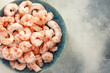 Close up frozen pilled shrimps with ice cubes on a blue plate on a blurred blue background with copy space. Prawns cooking. Frozen foods. Mediterranean, keto diet