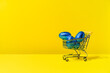© ADDICTIVE STOCK - A shopping cart with colourful blue foil eggs on a yellow background