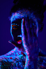 incognito black female with fluorescent prints on skin, cosmic paint glowing on neon lights, black background. young calm and peaceful lady losing half of face with hands, close-up