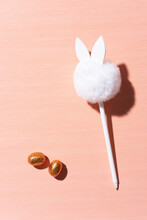 A White Pen With A Pompon On An Orange Background And Chocolate Eggs. The Pen Looks Like A Rabbit