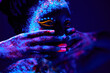 canvas print picture - close-up black female with fluorescent prints on skin, cosmic paint glowing on neon lights, black background in studio. female with body art closing half of face, touching. beauty, fashion concept