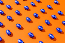 Pattern Of Blue Foil Chocolate Eggs On A Orange Background.