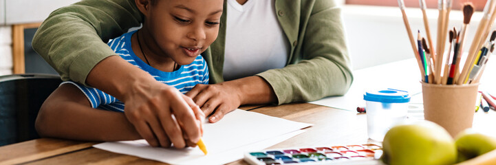 Wall Mural - Black woman drawing with her happy daughter at home kitchen