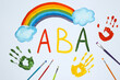 Drawn abbreviation ABA (Applied behavior analysis), rainbow, palm prints and paintbrushes on white paper, flat lay