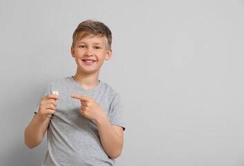 Poster - Little boy in grey t-shirt pointing at chewing gums on light background