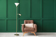 Comfortable armchair with pillow and floor lamp near color wall in room interior