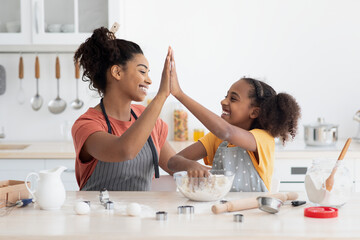 Wall Mural - Cheerful black mother and daughter giving high five while cooking