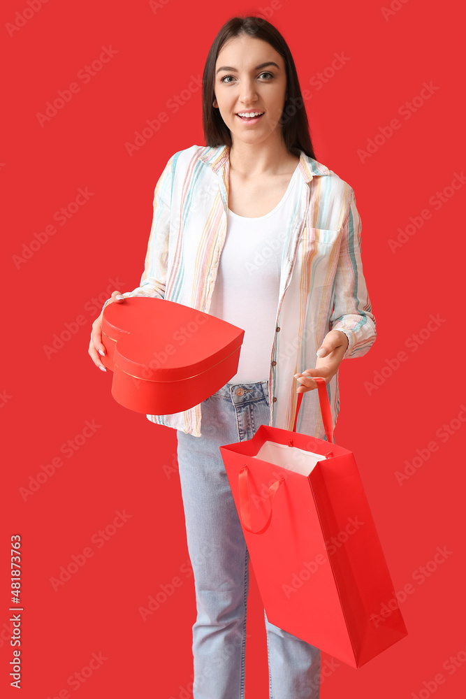 Young woman with shopping bag and box on red background