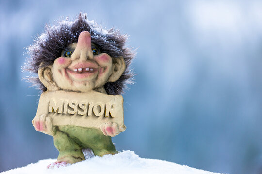 Happy troll holding sign with the word mission chiseled out. Soft blurred out background.