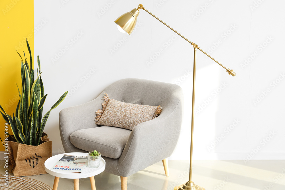 Golden standing lamp, armchair and table near light wall