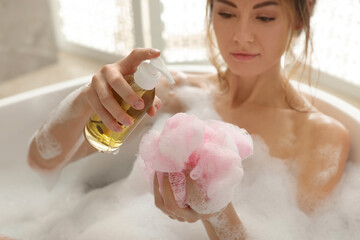 Wall Mural - Beautiful woman pouring shower gel onto mesh pouf in bath indoors, focus on hands