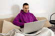 © Creative_Bird - Young caucasian man with violet hoodie sitting on bed and holding laptop computer. Man using notebook to surf in internet, read news, watch movie, study or work online, call friends. Relaxing at home.