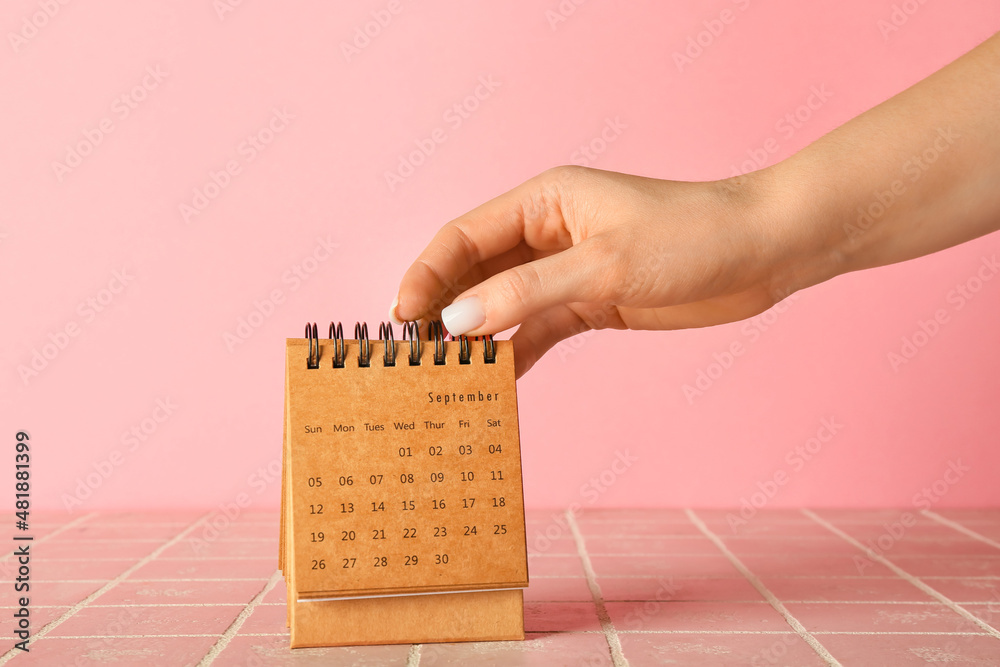 Female hand with craft calendar on pink background